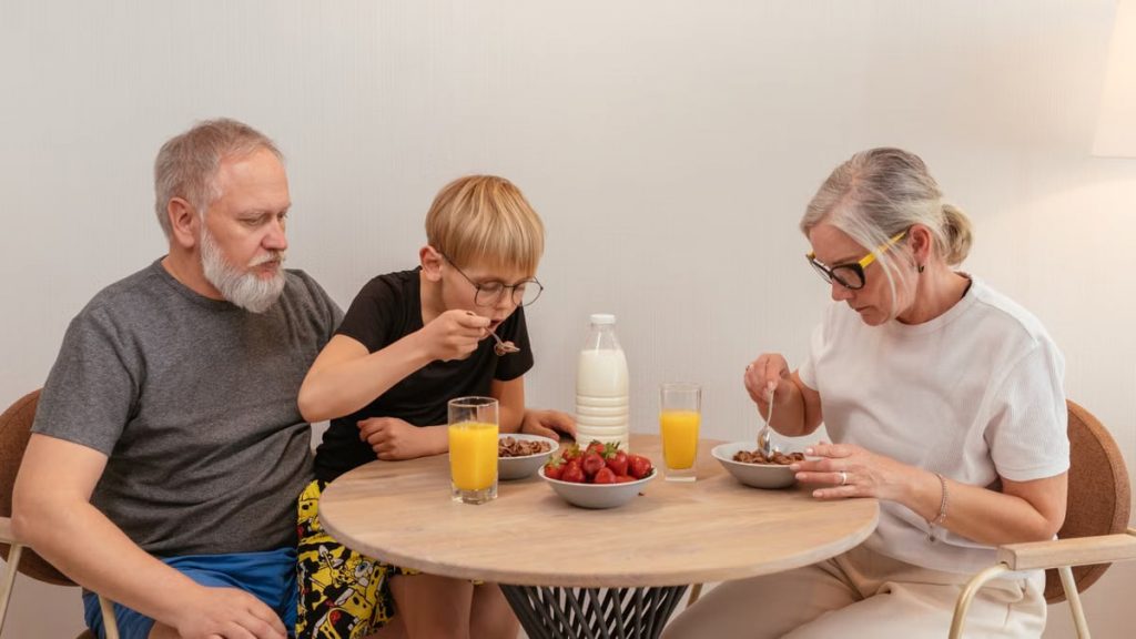 A family of three enjoying breakfast around a wooden table at home.
