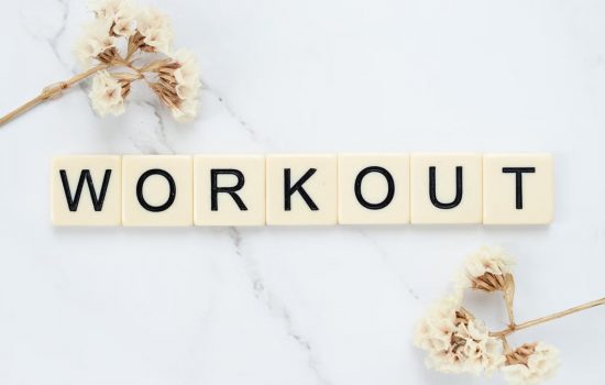 Letter tiles spelling 'WORKOUT' on marble with dried flowers, conveying fitness motivation.